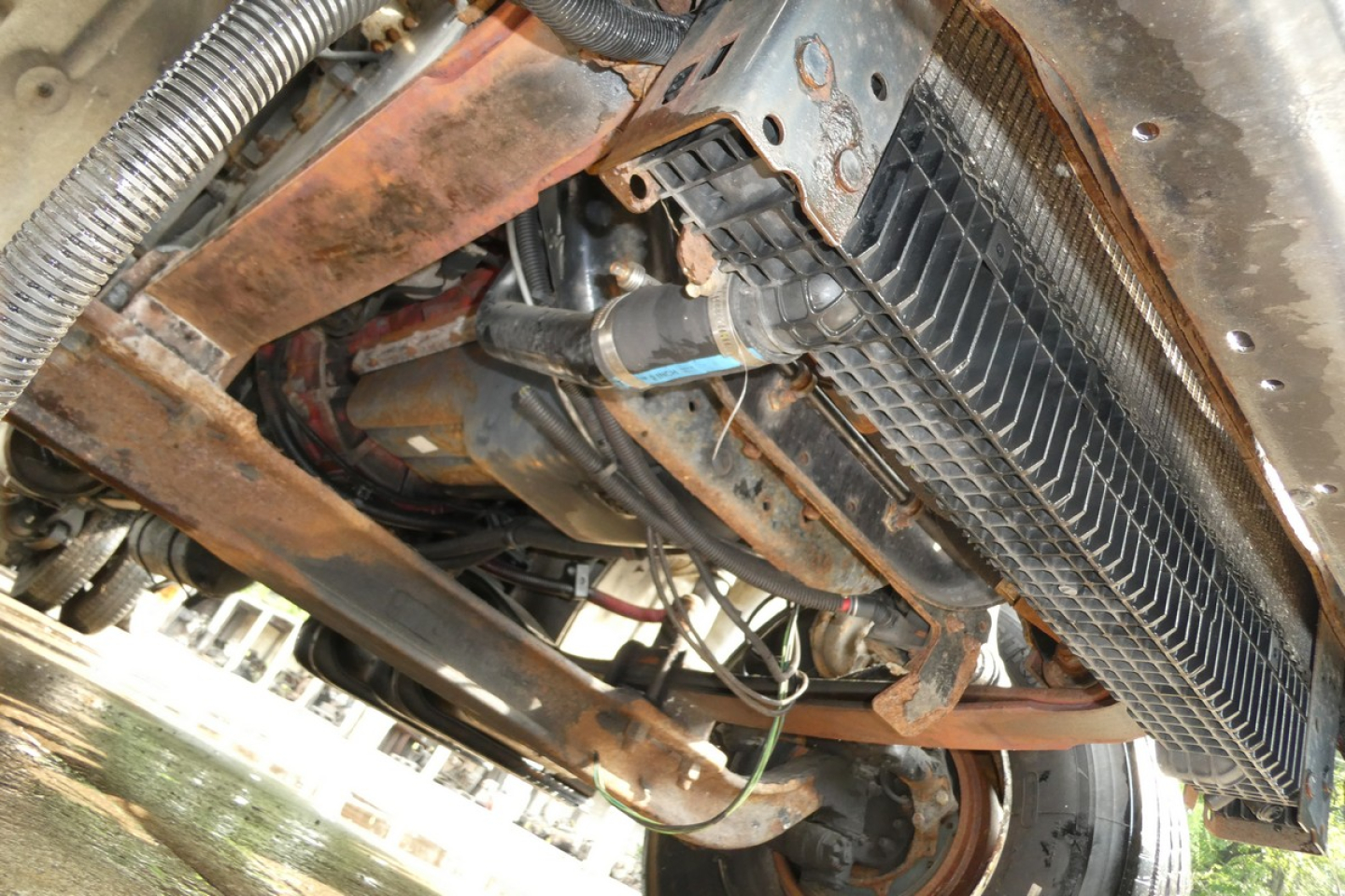 Truck chassis underside showing drivetrain, exhaust, and radiator with hoses visible.