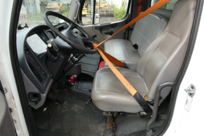 Cab interior of a 2008 Freightliner M2-106 showing grey vinyl seats, steering wheel, dashboard, and orange seat belt across the front seat.