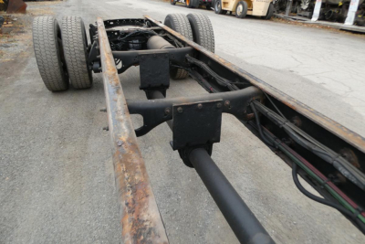 Chassis frame of a Freightliner M2-106 semi-truck showing dual rear axles, frame rails, and driveshaft with some surface rust.