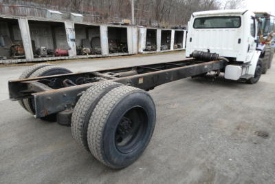 Freightliner M2-106 chassis showing rear dual wheels and long frame with cab in distance, white cab at right