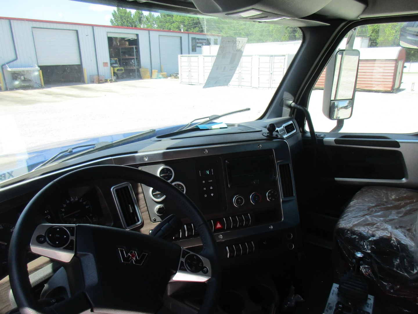 Interior cabin view of a new Western Star 49X dump truck showing steering wheel, dashboard, gauges, and driver seat covered with plastic.