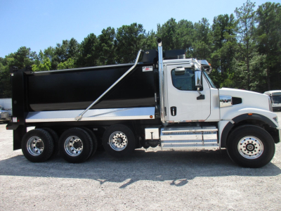 Dump truck side view with white cab and six-wheel dual rear axle. Black dump bed, chrome steps, fuel tanks, and branding on door.