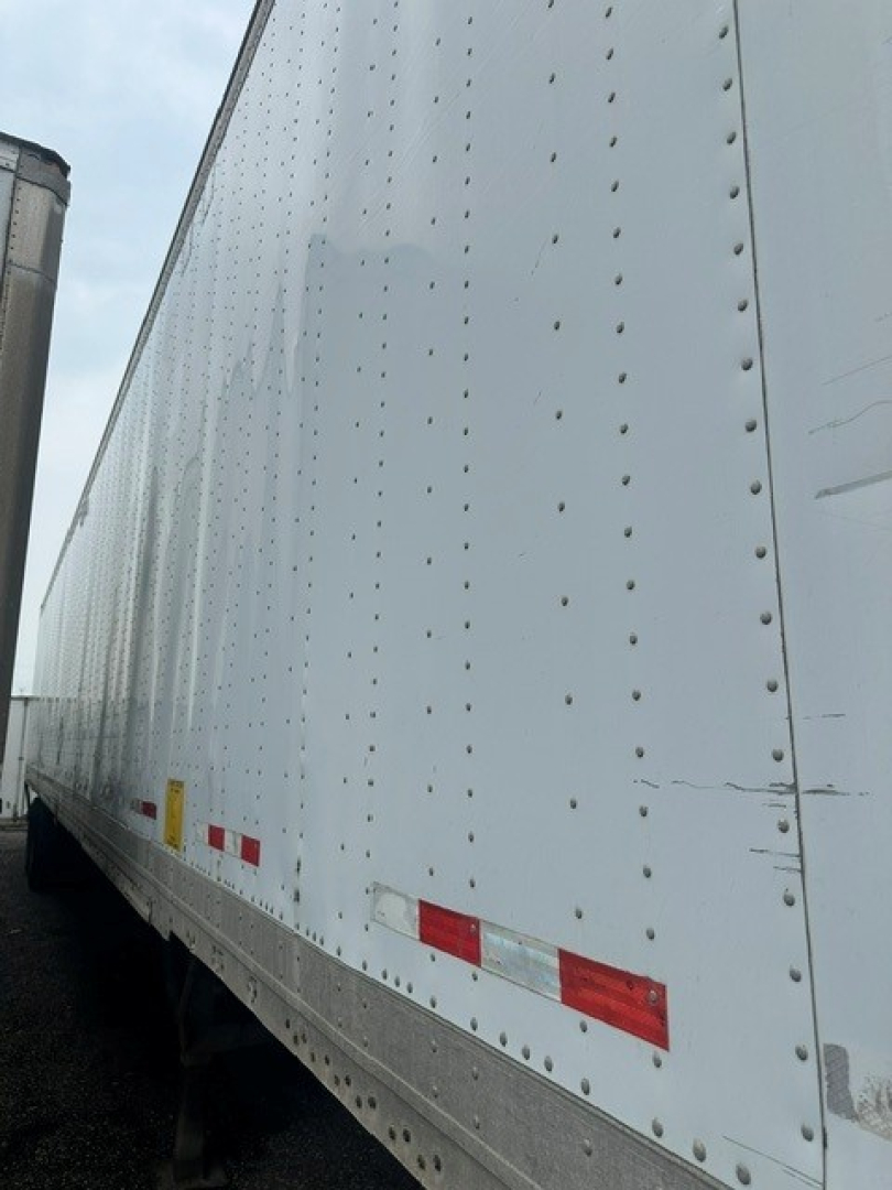Trailer side showing riveted white dry van with reflectors and trailing edge, platform and corner details visible.
