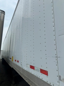 Trailer side showing riveted white dry van with reflectors and trailing edge, platform and corner details visible.