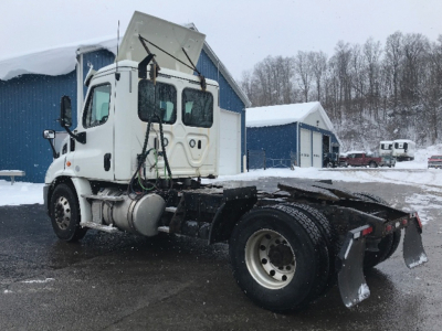 2018 Freightliner Cascadia 113 daycab rear view showing chassis and dual rear axles with snow, side mirrors, and cab tilt open.