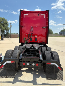 Rear view of a red Kenworth truck sleeper cab tractor showing the fifth wheel, dual rear axles, mud flaps, and bumper with lights and wiring harnesses.