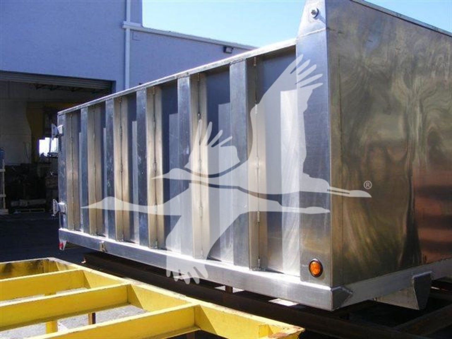 Dump truck bed showing metal sides and small orange signal light with a graphic of a bird in flight on the side panel.