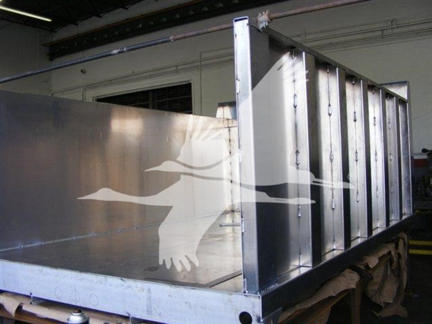 Dump truck bed shown in a new Advanced Fabricators 12 ft chassis with shiny metal sides and vertical ribs.