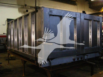 Dump truck bed or trailer in a workshop setting with structural metal sides and a logo overlay of flying geese.
