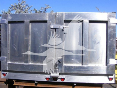 Back of a dump truck trailer showing solid metal doors, latch, and lights; no visible text on the unit itself.
