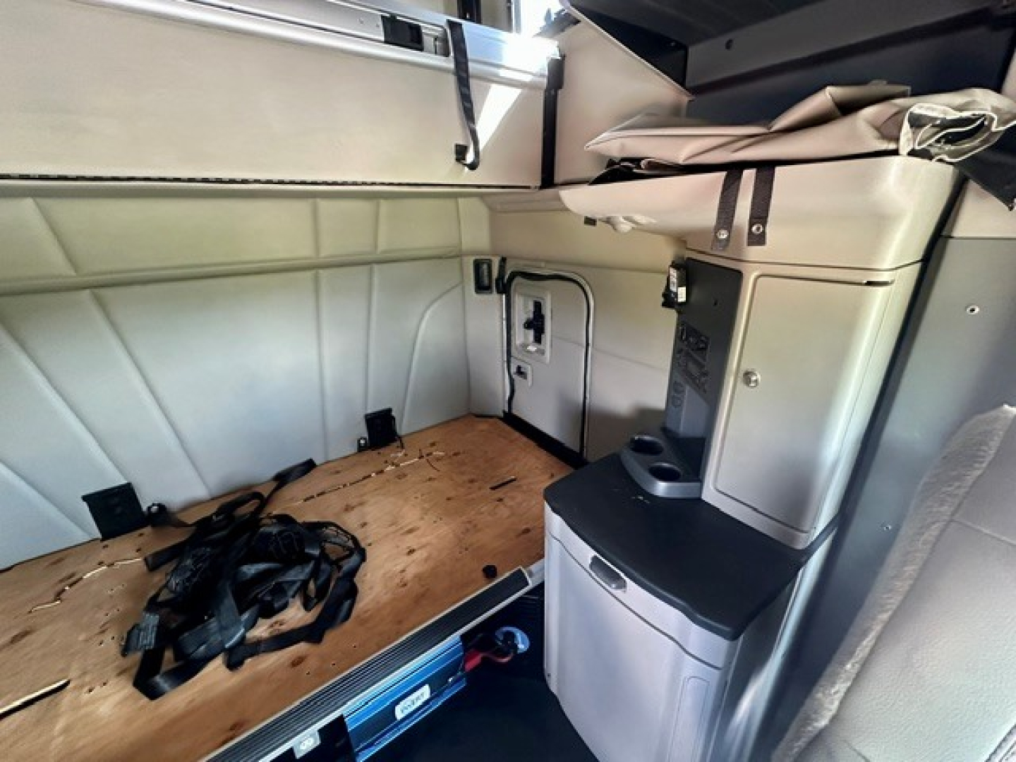 Peterbilt 579 cab interior overview showing sleeper area with wooden floor panel and seat console; USB/storage area and utility access panel visible.