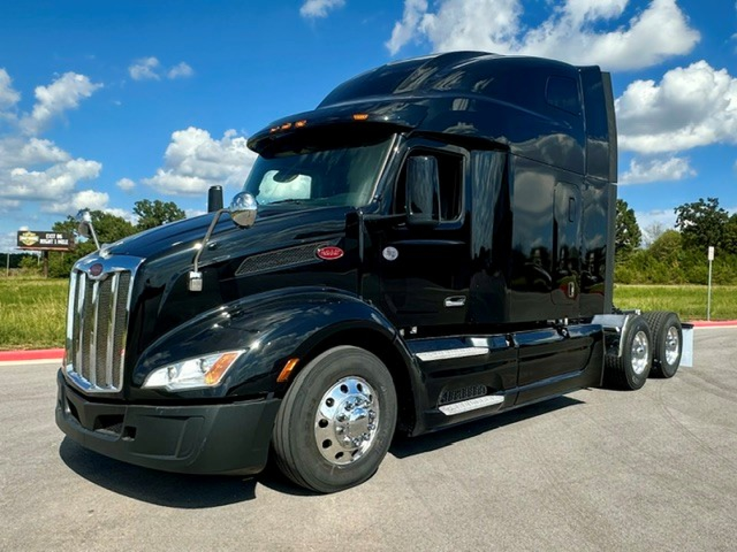 Peterbilt 579 conventional sleeper truck, black exterior, front three-quarter view, chrome wheels, dual rear axles, cab high-roof, on pavement with blue sky