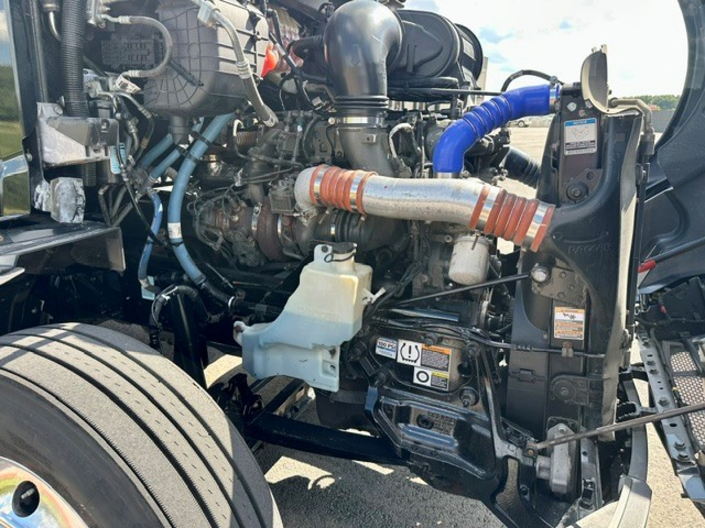 Peterbilt 579 engine bay with visible intake piping, radiator, hoses, coolant reservoir, and various engine components.