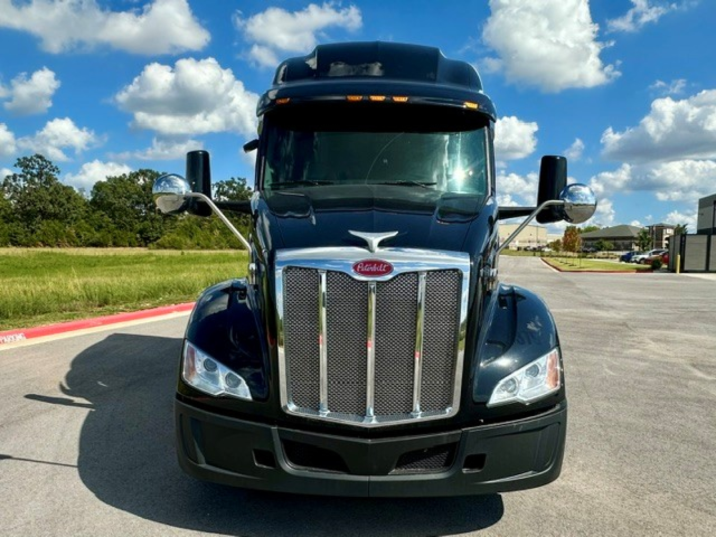 Peterbilt 579 truck facing camera, chrome grille, black body, tall sleeper cab, clear blue sky with clouds.