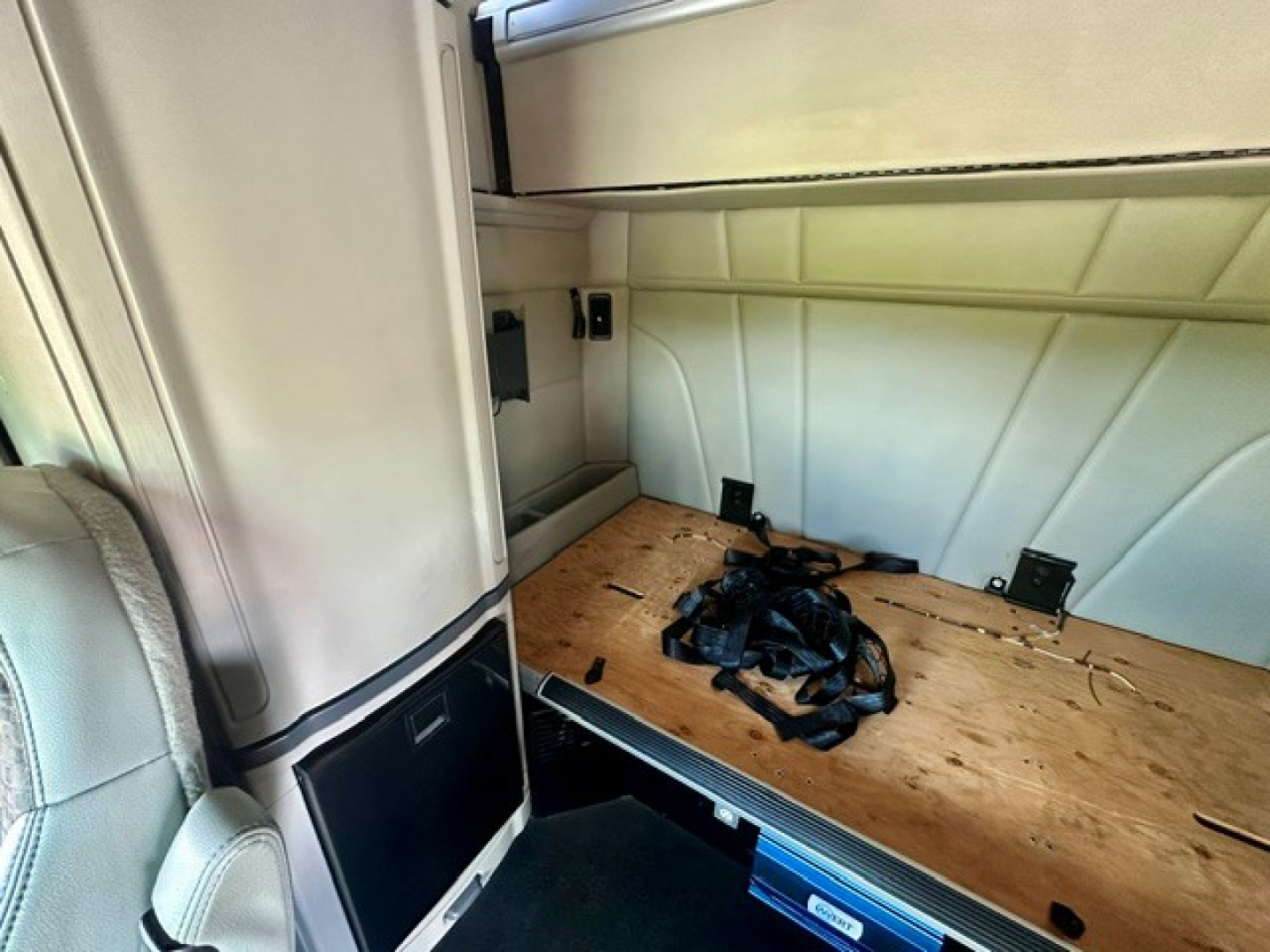 Peterbilt 579 sleeper truck interior cargo area with wooden floor and seat visible, cargo straps on the bed, Hinged wall panels in view.