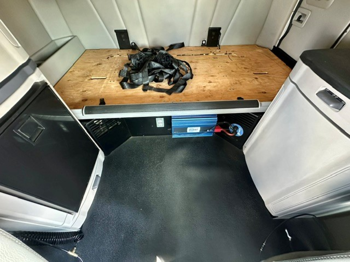 Peterbilt 579 sleeper cab interior cargo area showing wooden floor and storage with seat belts, battery box, and side cabinets visible.