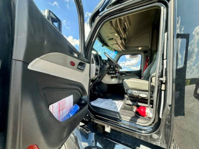 Peterbilt 579 truck cab interior view from open driver's door showing dashboard, steering wheel, and seating area.