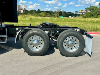 Dual rear wheel assembly of a Peterbilt semi-truck chassis with chrome hubs and tire treads visible; part of fifth wheel and frame assembly, road in background.