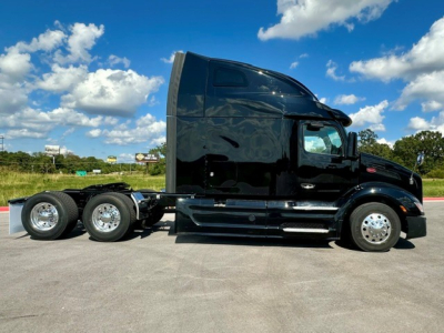 Side view of a black 2022 Peterbilt 579 conventional sleeper truck, showing twin rear axles, chrome wheels, and aerodynamic styling.