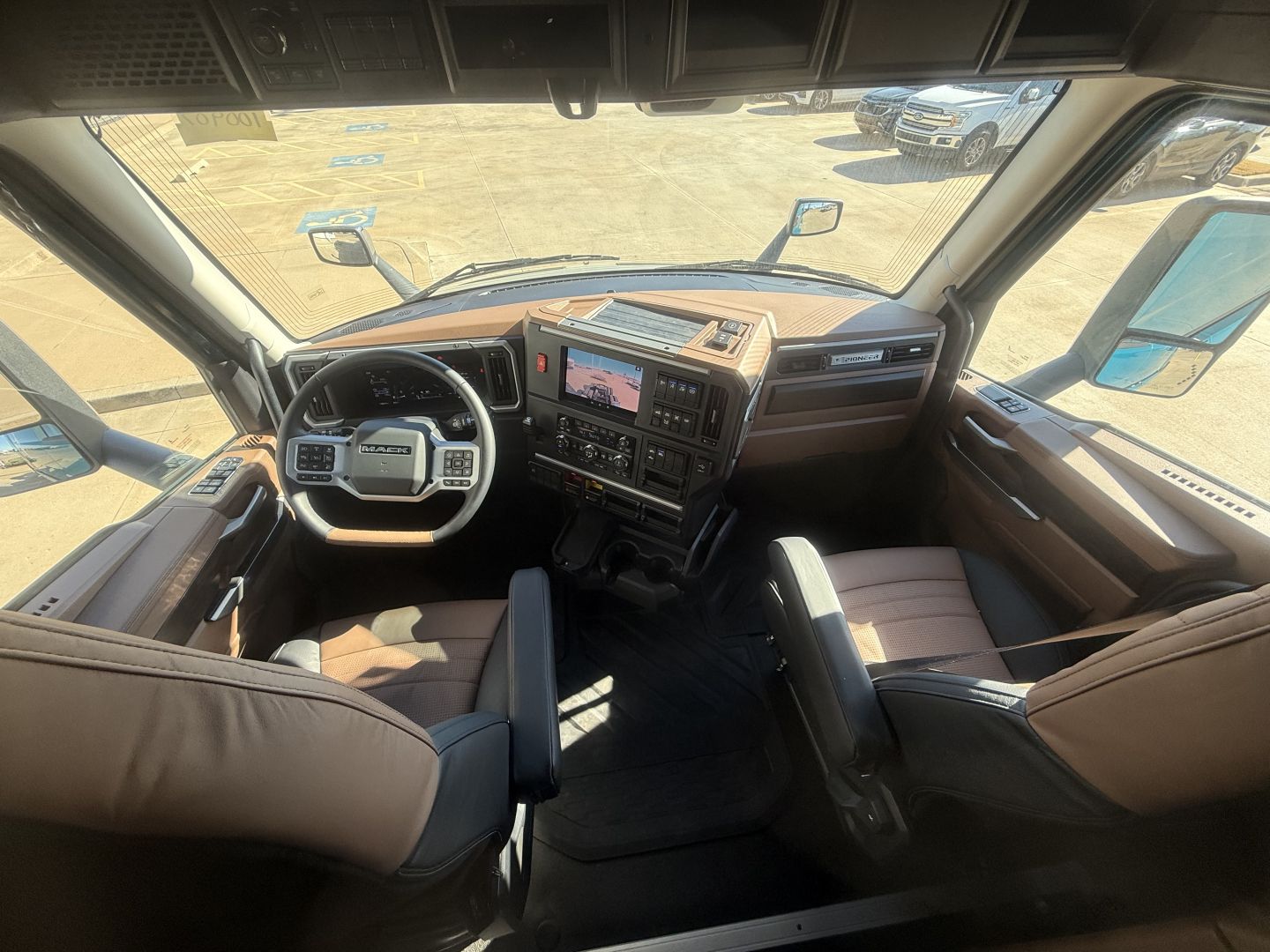 Truck cab interior showing steering wheel, dashboard, and driver's seat of a new Mack PR64T76H sleeper tractor.