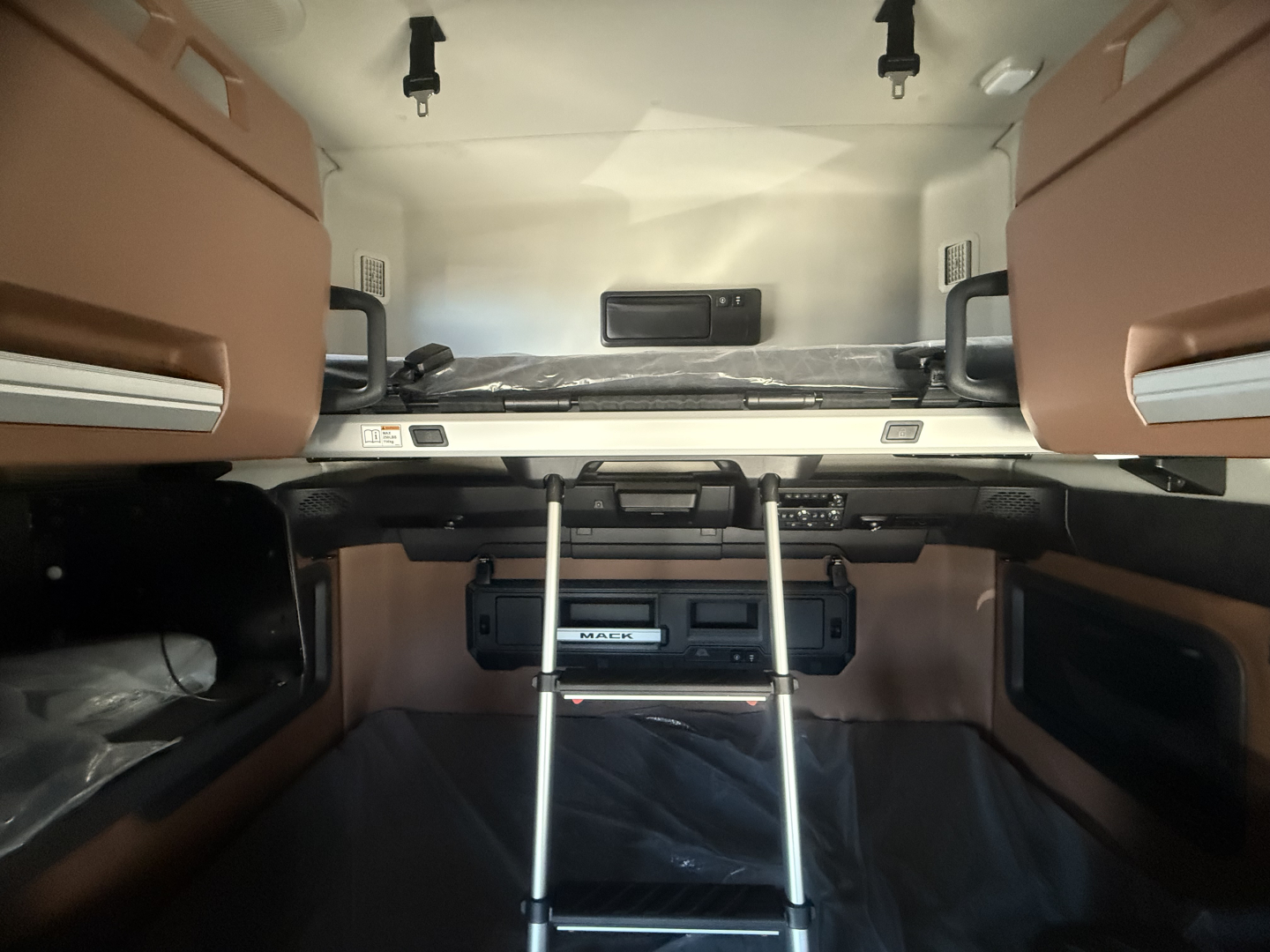 CAB interior of a new Mack PR64T76H sleeper showing bunk beds, ladder, and dashboard with storage compartments.