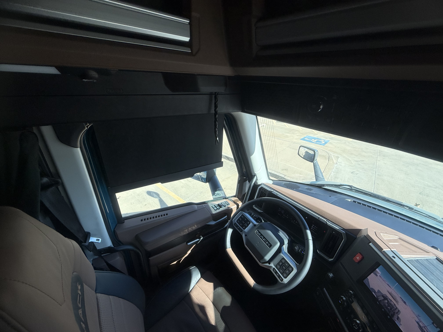 Mack PR64T76H cab interior showing steering wheel and dashboard with large side window and visor.