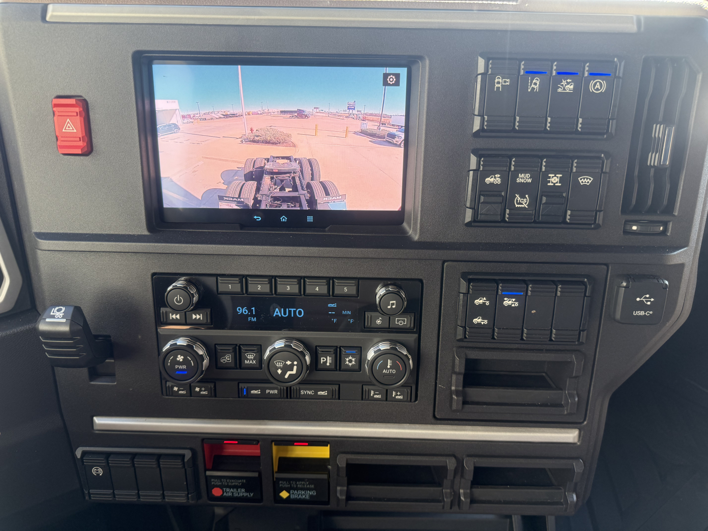 Dashboard center showing a display screen and climate controls in a Mack PR64T76H truck cab with multiple control panels.