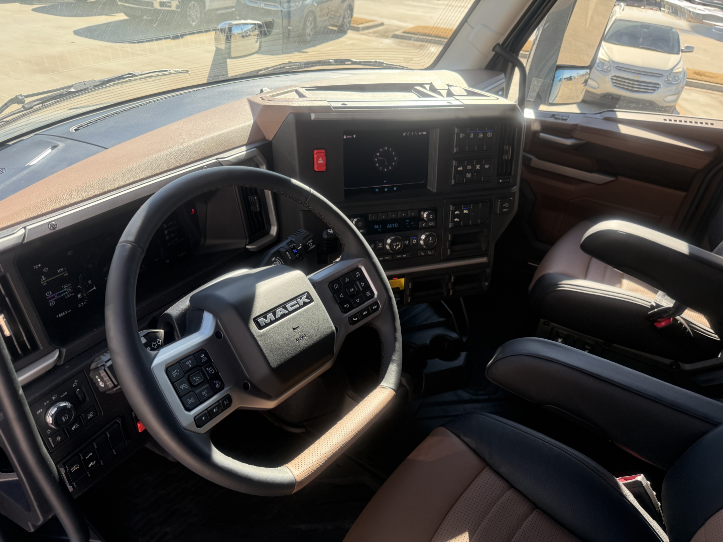 Mack PR64T76H truck cab interior showing steering wheel and dashboard with controls and brown seating.