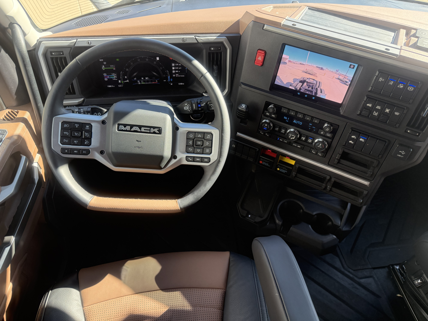 Mack PR64T76H truck cab interior showing steering wheel and dashboard with digital gauge cluster and touchscreen display.