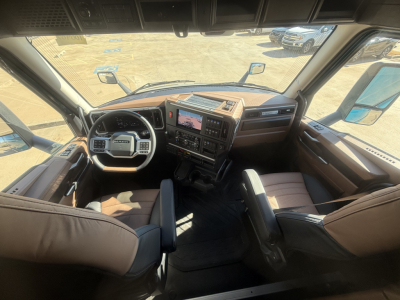 Truck cab interior showing steering wheel, dashboard, and driver's seat of a new Mack PR64T76H sleeper tractor.