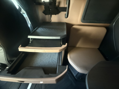 Truck cab interior showing open storage drawers under a fold-down step, with beige seat and black panels.