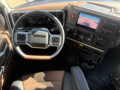 Mack PR64T76H truck cab interior showing steering wheel and dashboard with digital gauge cluster and touchscreen display.