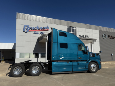 Truck cab and chassis in blue showing Mack PR64T76H sleeper cab with large side fairing and chrome wheels at dealership