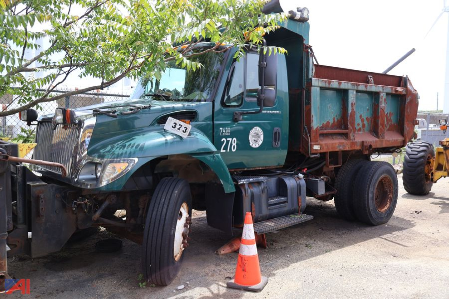 Green 2005 International WorkStar 7400 dump truck with orange dump bed, front left wheel missing, traffic cone nearby, side decals and numbers visible.