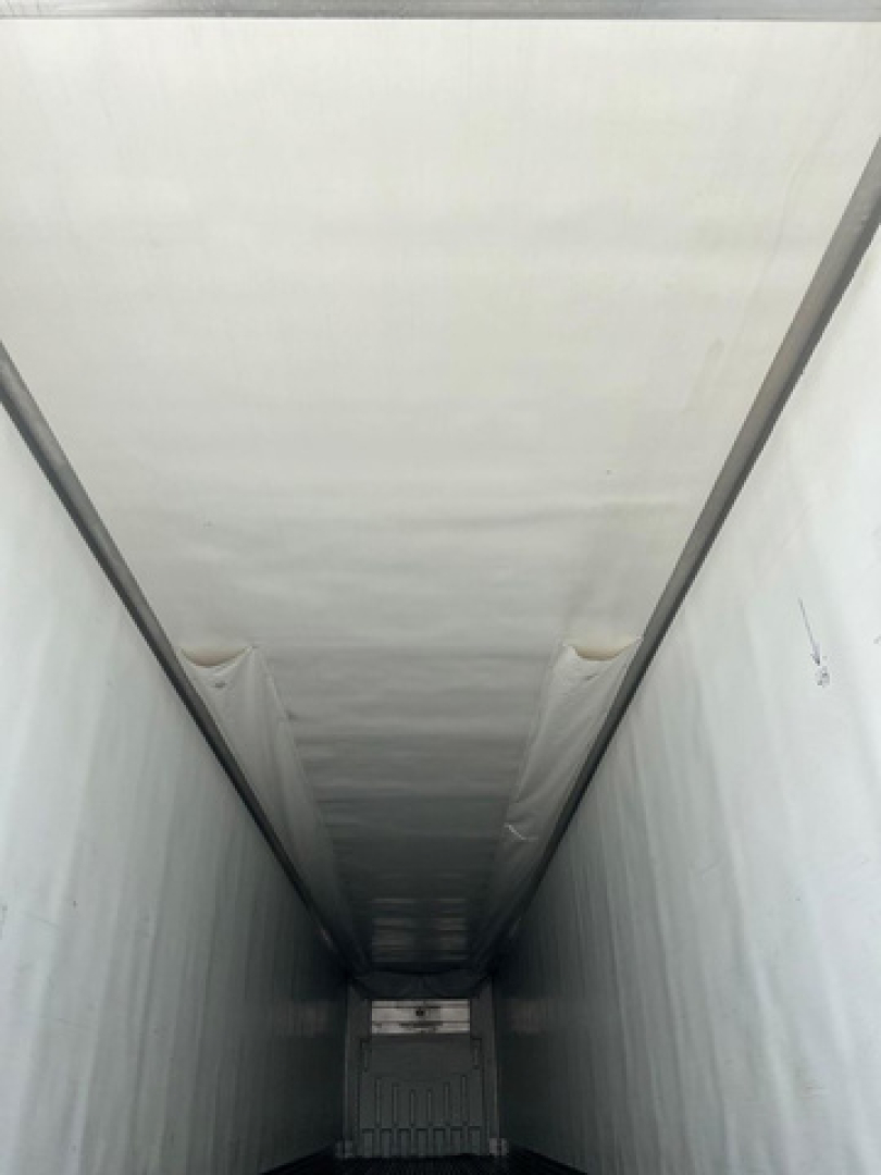 Interior view of a refrigerated trailer cargo area with white insulated walls and ceiling, long narrow tunnel leading to rear doors.