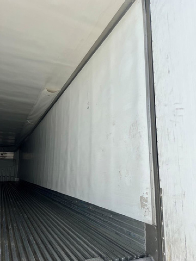 Trailer interior showing white insulated wall and ribbed floor of a refrigerated trailer, door opening visible at right.