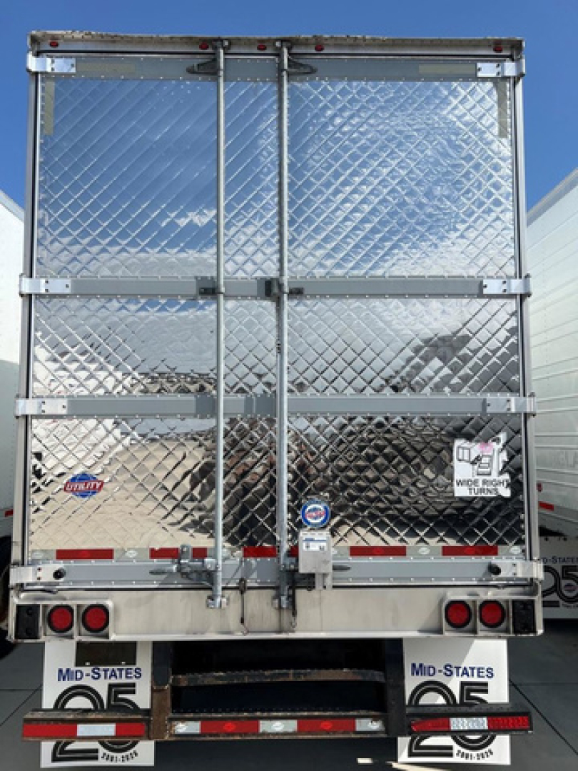 Refrigerated trailer rear showing diamond plate doors with latches, bumper lights, and license plates; various stickers and reflectors visible.