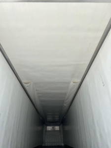 Interior view of a refrigerated trailer cargo area with white insulated walls and ceiling, long narrow tunnel leading to rear doors.