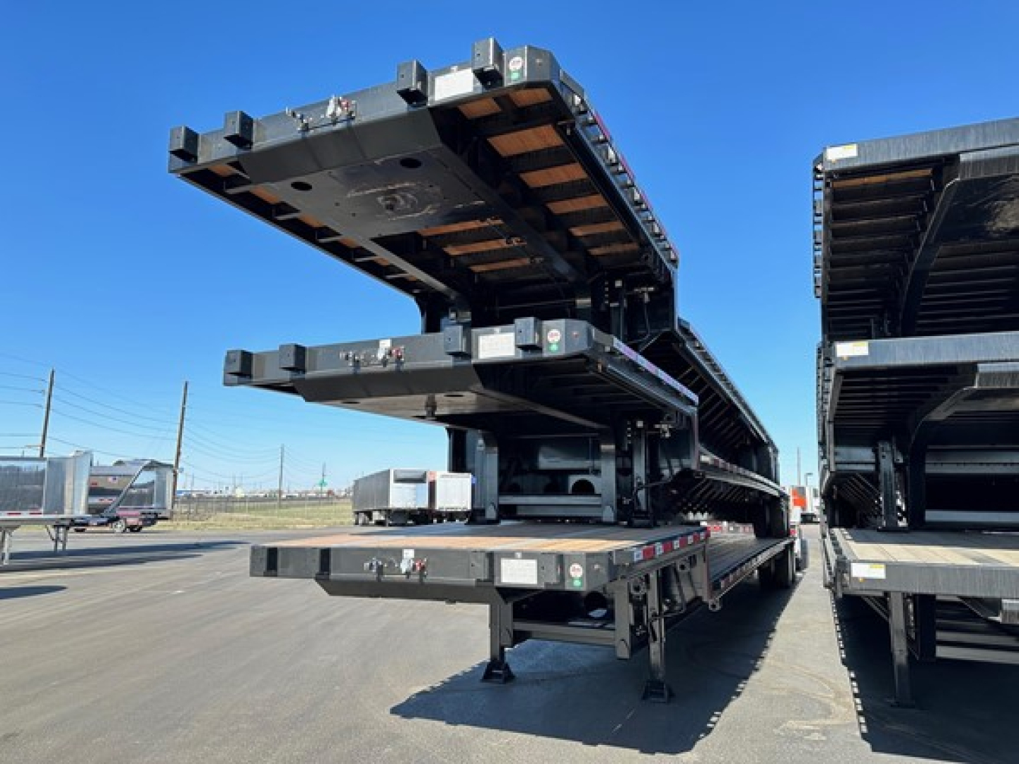 Drop deck trailers stacked on a multi-axle trailer in a yard showing black steel frame and wooden deck components.