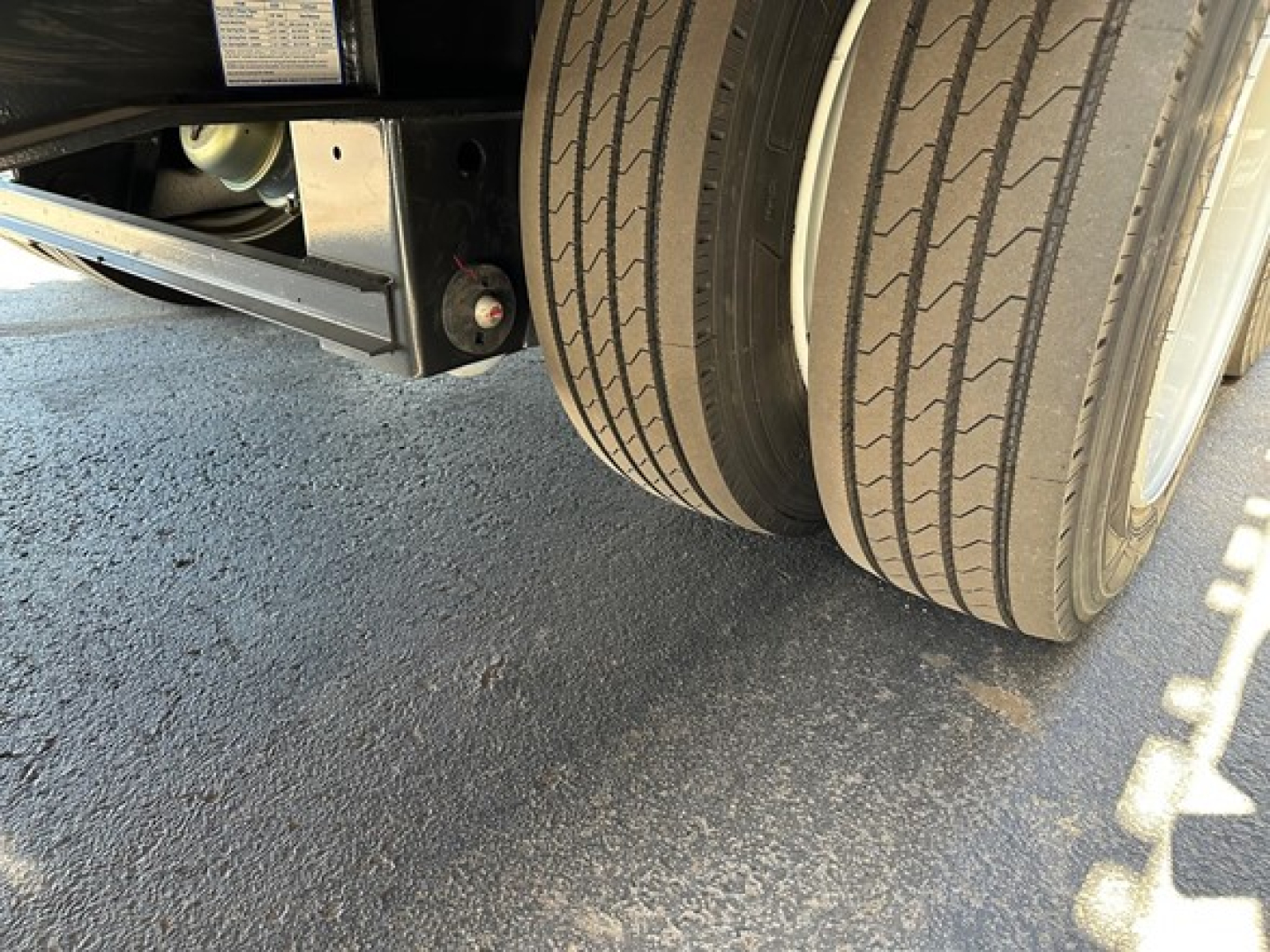 Drop deck trailer wheel area showing dual tires and undercarriage components with a label plate.