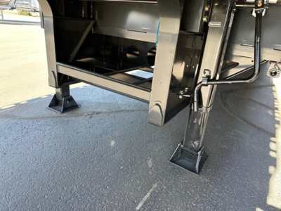 Trailer landing gear and undercarriage of a new drop deck trailer with metal frame, support legs, and black components. Visible hardware and structural members.