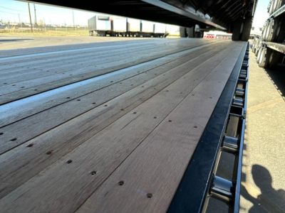 Drop deck trailer bed with wooden planks and steel edge, low-angle view along platform with wheel at far end.