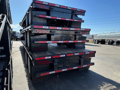 Drop deck trailers stacked vertically showing black steel frames with red and white reflective markings.