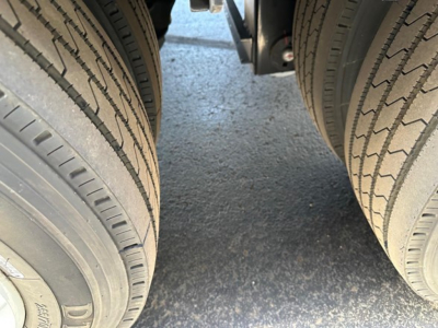 Truck trailer tires and part of the undercarriage for a Dura Haul drop deck trailer. Close-up view of dual rear axles with treaded tires.