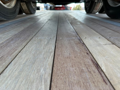 Wide view of a trailer deck from between wheels, showing wooden planks and rails; no legible labels or text visible on the deck.