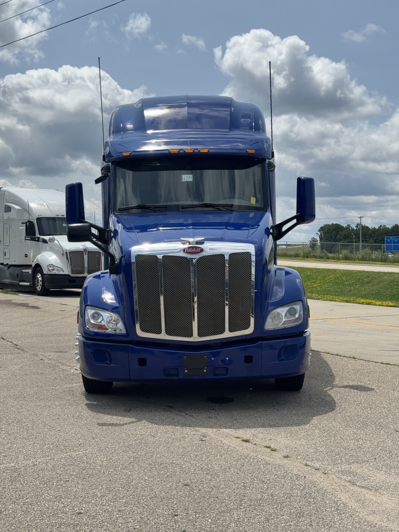 Peterbilt 579 conventional sleeper truck in blue, front view, with large chrome grille, dual mirrors, and tall aerodynamic hood.
