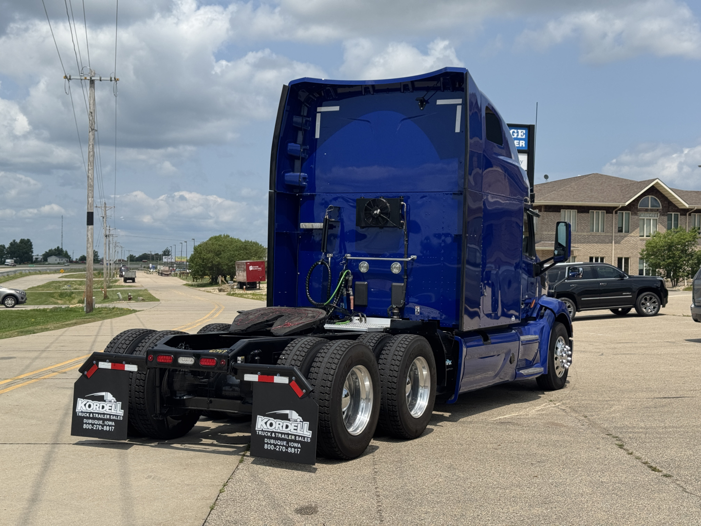 Truck rear view of a blue Peterbilt 579 sleeper cab tractor showing dual rear axles and mud flaps with Kordell dealership plates.