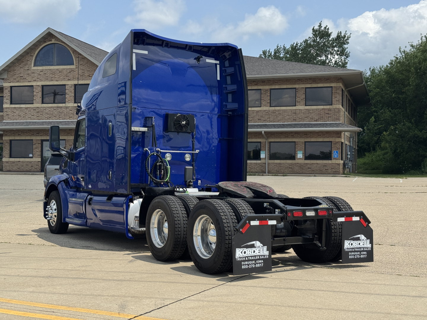 Peterbilt 579 sleeper cab tractor rear view showing dual rear axles and aerodynamic blue paint; visible exhaust system, wheels, and mud flaps with company branding.