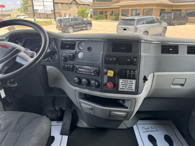 Peterbilt 579 dashboard and steering wheel interior showing instrument cluster, center console with radio, climate controls, and multiple switches; front passenger area with glove box and folders on floor.