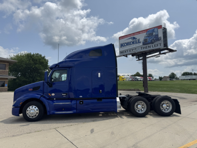 Peterbilt 579 tractor unit in blue, side view showing sleeper cab, two rear axles and fifth wheel, no trailer attached.